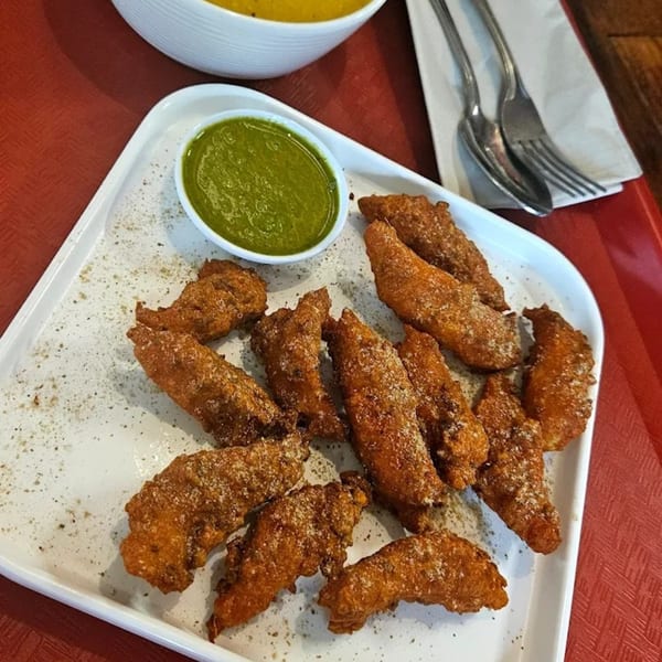 Crispy fried Indian chicken pakora with green chutney on a white platter at Hamara Restaurant.