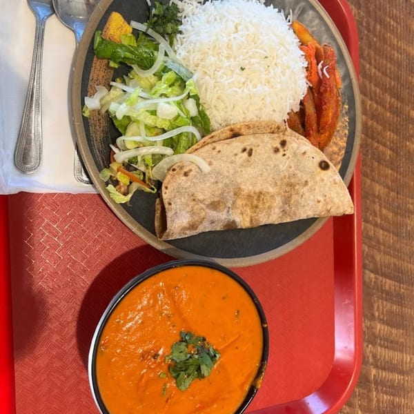 Indian meal with rice, salad, flatbread, and a side of orange curry on a red tray.