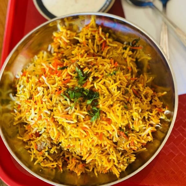 A close-up of a metal bowl filled with colorful Indian biryani, garnished with fresh cilantro.