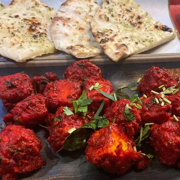 Bright red Indian chicken tikka pieces with green herbs and naan bread on a wooden tray.