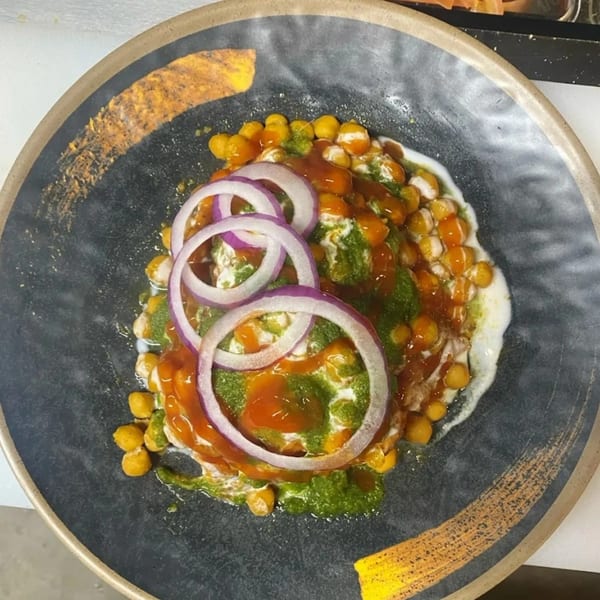 Hamara Restaurant's Indian chaat with chickpeas, sauces, yogurt, and red onion on a dark plate.