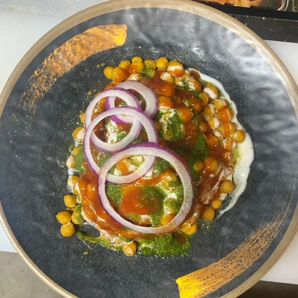 A Hamara Restaurant Indian dish with chickpeas, red onions, and green and red sauces on a dark plate.